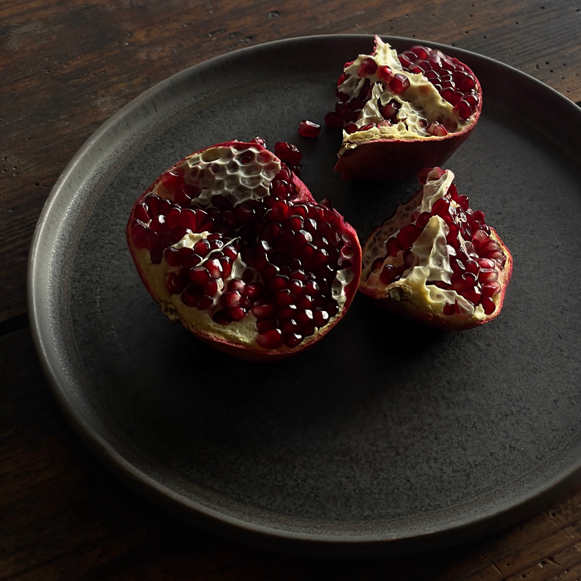 Brauner Keramik Teller mit einem Granatapfel auf einem Holztisch